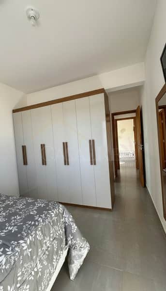 Quarto com armário grande embutido, cama com colcha estampada e piso cinza. Ambiente clean e organizado.