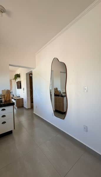 Sala clara com espelho orgânico na parede. Piso cinza e armários brancos visíveis.