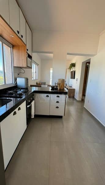 Cozinha moderna com armários brancos e bancada preta, integrada à sala de estar. Piso cerâmico claro.