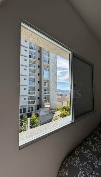 Quarto com janela ampla e vista para prédio moderno. Boa iluminação natural e ventilação.