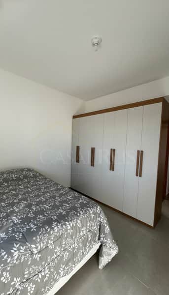 Quarto com cama de casal e armário grande embutido com portas brancas e detalhes em madeira. Ambiente claro e organizado.