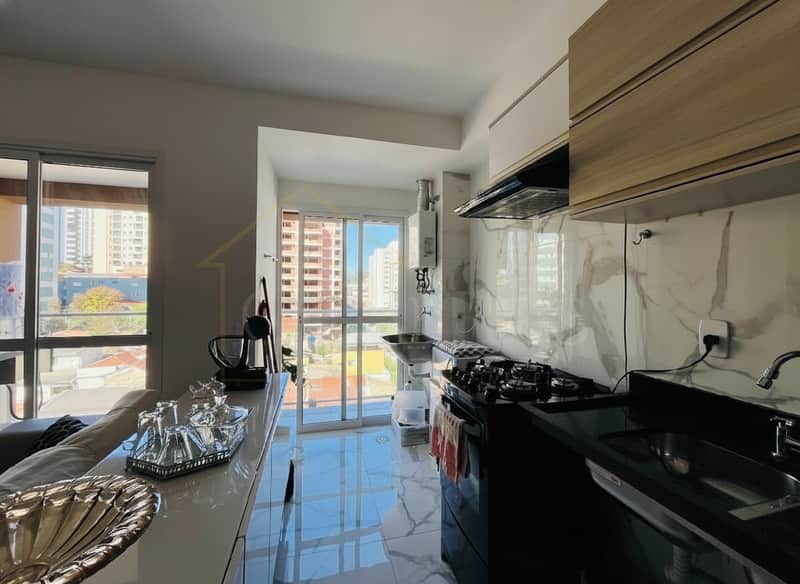 Cozinha moderna com armários claros, fogão preto e pia inox. Piso em mármore claro e janela com vista da cidade.