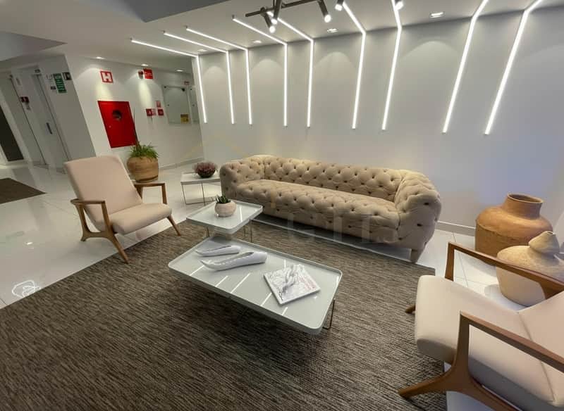 Sala de estar moderna com sofá bege, poltronas claras, tapete texturizado e iluminação linear no teto.