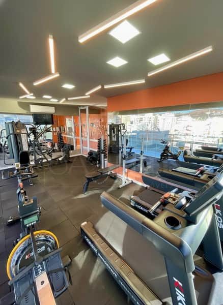 Academia moderna com equipamentos de ginástica, piso preto e vista panorâmica da cidade.