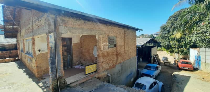 Fachada de casa antiga com tijolos aparentes e carros. Construção simples com área externa.