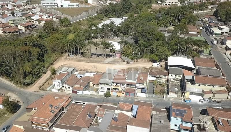Visão aérea de casas com telhados marrons, área verde e rua movimentada. Destaque para painéis solares.