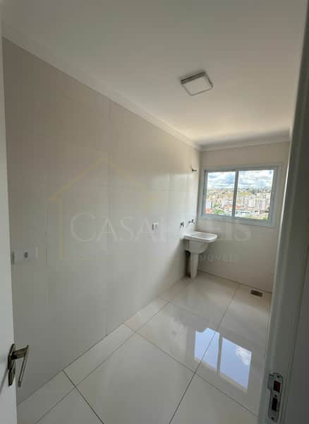 Área de serviço clara com pia, azulejos brancos e janela com vista da cidade. Piso brilhante.