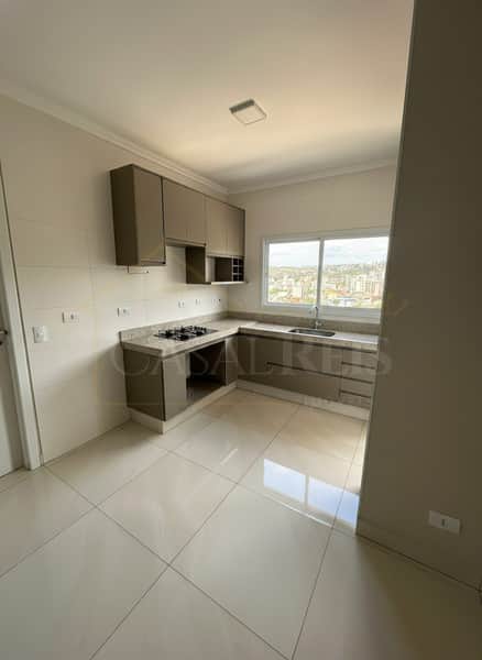 Cozinha clara com armários cor de terra, bancada em granito e piso cerâmico. Janela com vista da cidade.