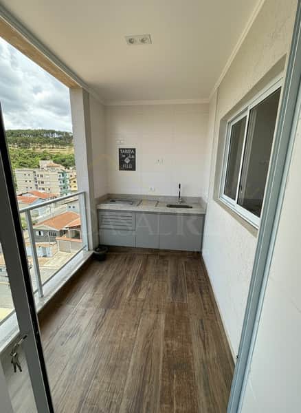 Varanda gourmet com armários planejados, pia, piso amadeirado e vista da cidade.