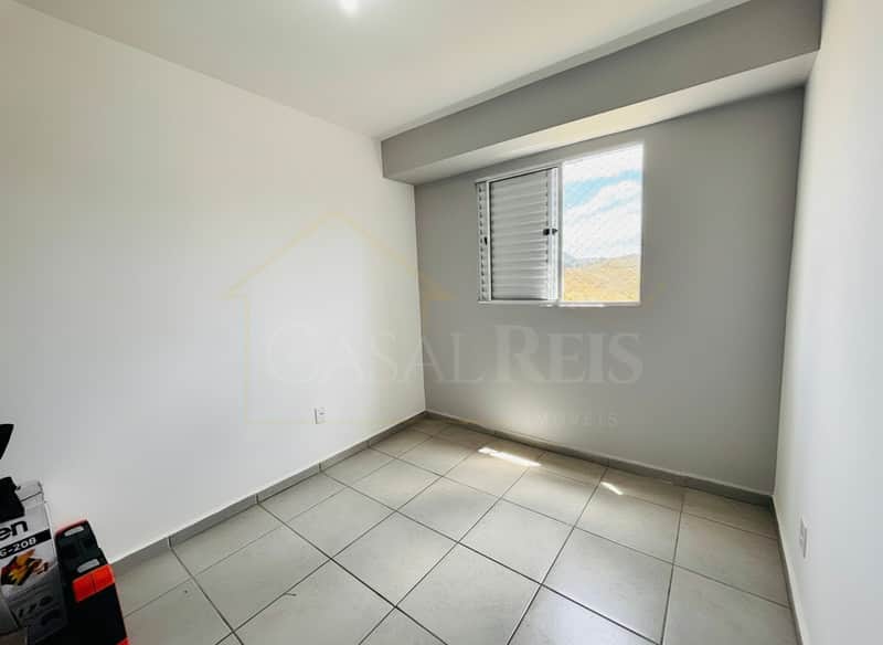 Quarto vazio com piso cerâmico e janela com veneziana. Paredes claras e iluminação natural.