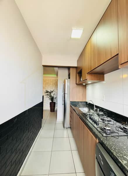 Cozinha estreita com armários amadeirados, bancada escura com cooktop e parede decorada em preto e branco.