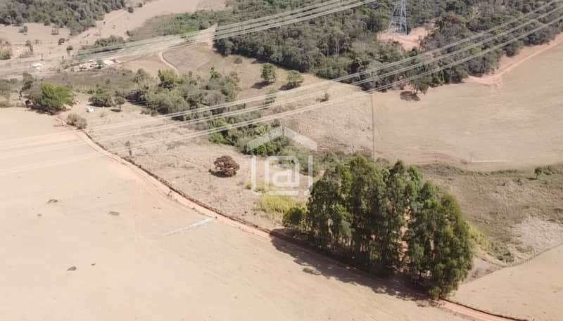 Área externa rural com vegetação, pasto seco e rede de energia. Vista aérea ensolarada.