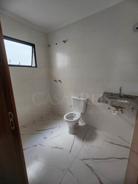 Banheiro claro com piso de mármore, vaso sanitário branco e pia com bancada de granito. Janela com moldura preta.