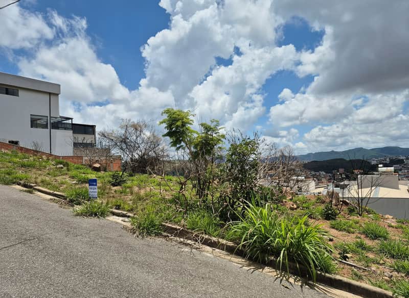 Terreno em declive com vegetação, vista para a cidade e céu azul com nuvens.
