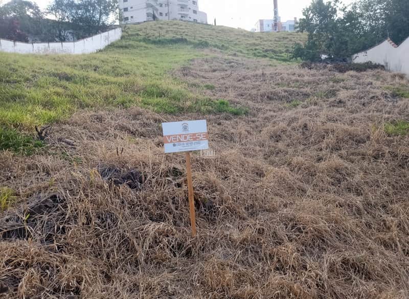 Terreno à venda em declive com vegetação seca. Placa "Vende-se" em destaque. Ideal para construção.