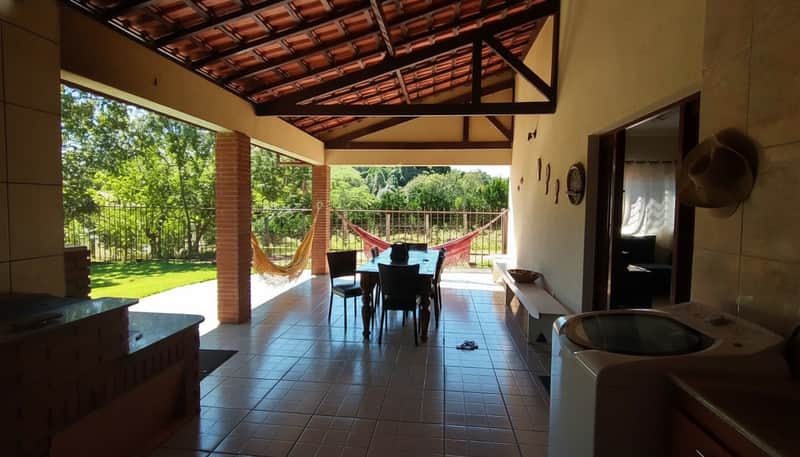 Varanda ampla com mesa, cadeiras e churrasqueira. Vista para o jardim e área verde. Decoração rústica e aconchegante.