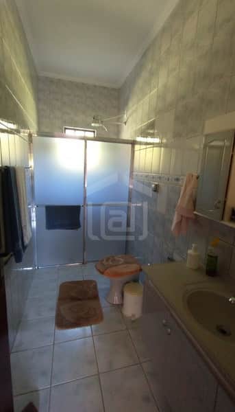 Banheiro com azulejos cinzas, box de vidro fosco, pia com armário e vaso sanitário com tampa estampada.