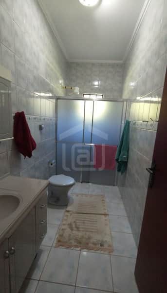 Banheiro com azulejos claros, pia com gabinete, vaso sanitário e box com cortina translúcida.