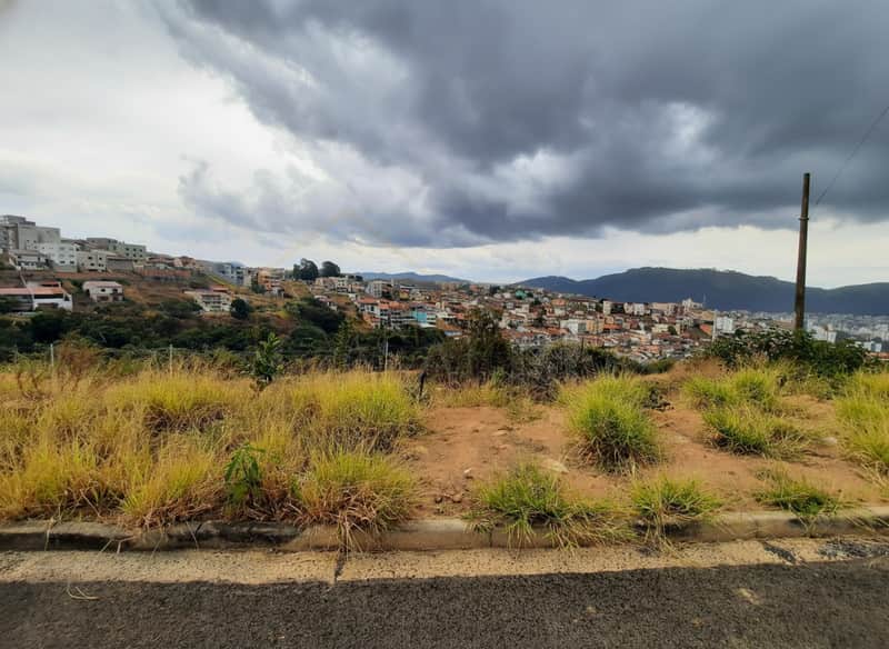 Terreno com vista urbana sob céu nublado. Vegetação rasteira e construções ao fundo.