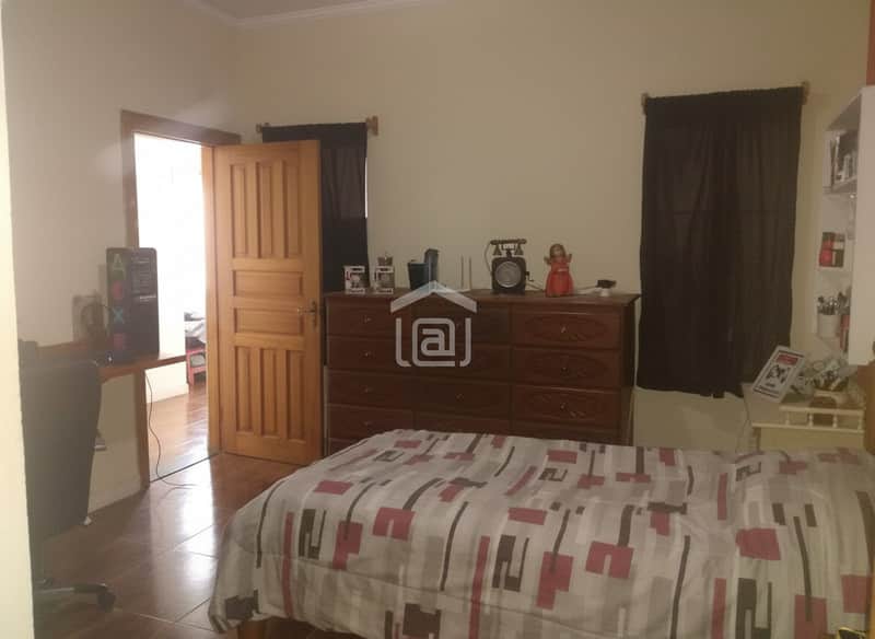 Quarto com cama de casal, cômoda de madeira escura e cortinas pretas. Decoração vintage.