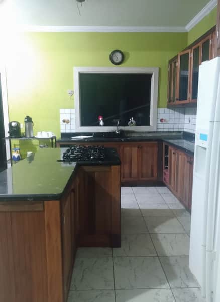 Cozinha ampla com ilha central, armários de madeira e piso claro. Ambiente bem iluminado e organizado.