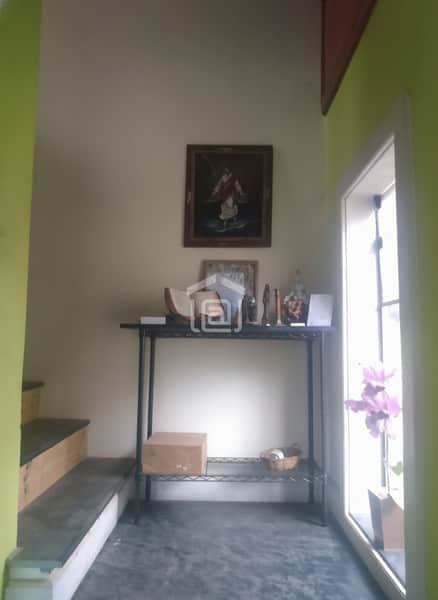 Hall de entrada com escada, mesa de metal, objetos decorativos e quadro na parede. Ambiente iluminado.