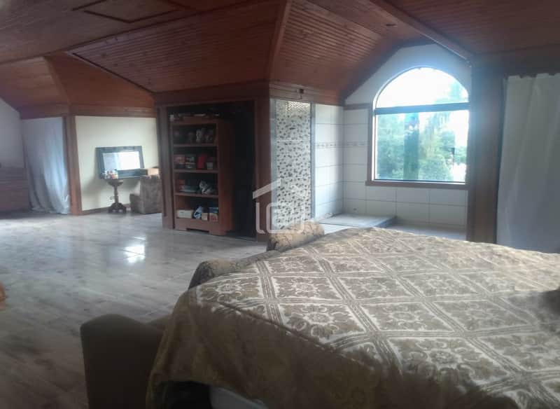 Quarto amplo com teto de madeira, cama grande, janela e armário embutido. Piso brilhante e decoração clássica.