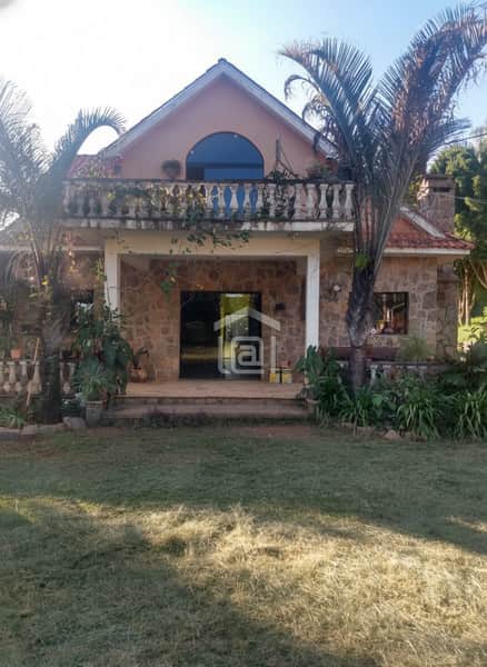 Fachada de casa rústica com varanda, pedras e palmeiras. Jardim gramado. Arquitetura charmosa.