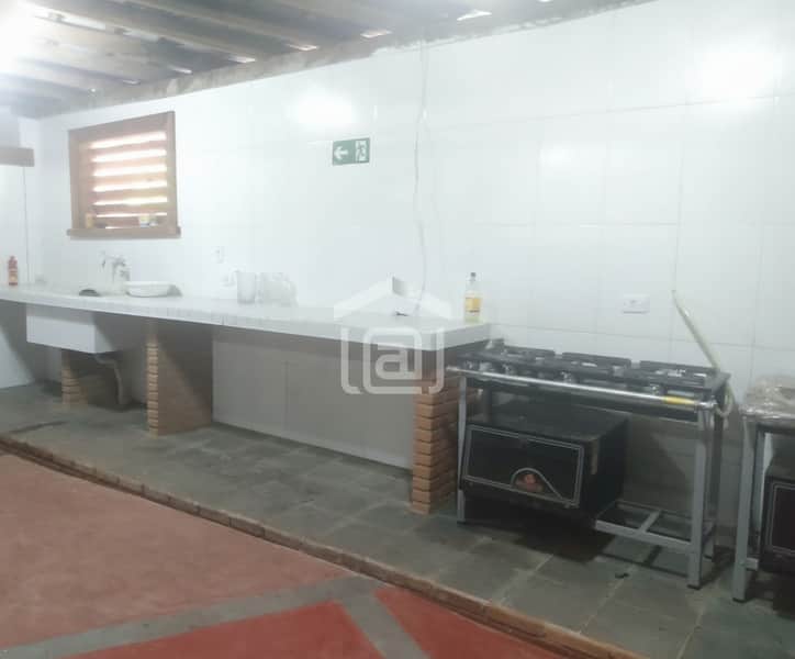 Cozinha ampla com bancada, pia, fogão industrial e piso rústico. Ambiente claro e funcional.