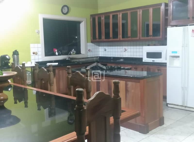 Cozinha ampla com armários de madeira, bancada escura, mesa com cadeiras e geladeira branca.