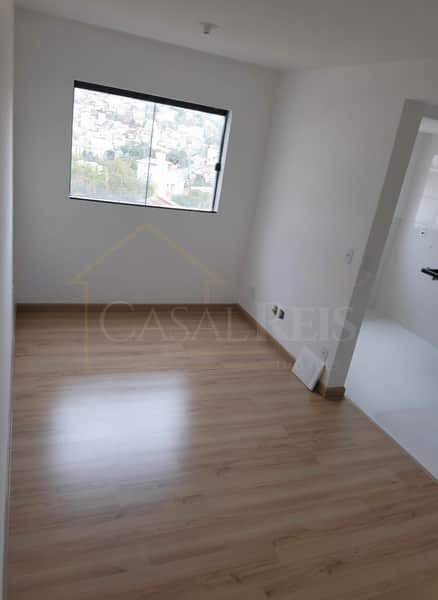 Sala clara com piso laminado e janela. Ambiente arejado, com paredes brancas e detalhes minimalistas.