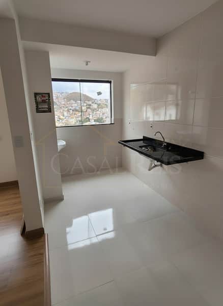 Cozinha clara com pia preta suspensa, azulejos brancos e janela com vista para a cidade. Piso branco brilhante.