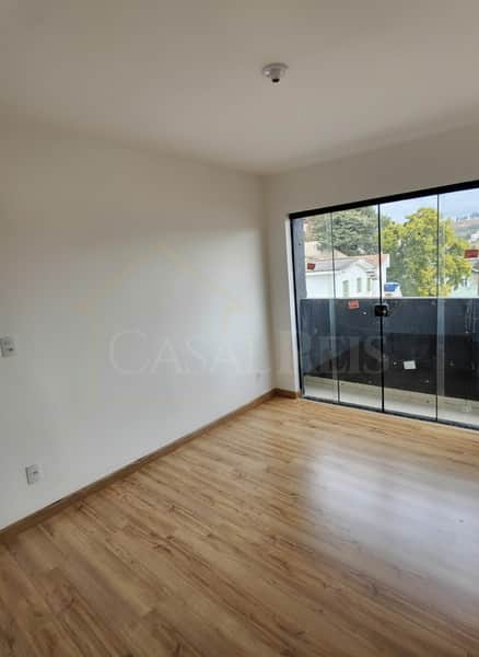 Sala clara com piso amadeirado e porta de vidro para varanda. Ambiente arejado e iluminado.