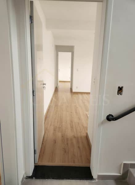 Interior de imóvel com piso amadeirado, paredes brancas e porta aberta para outro cômodo.
