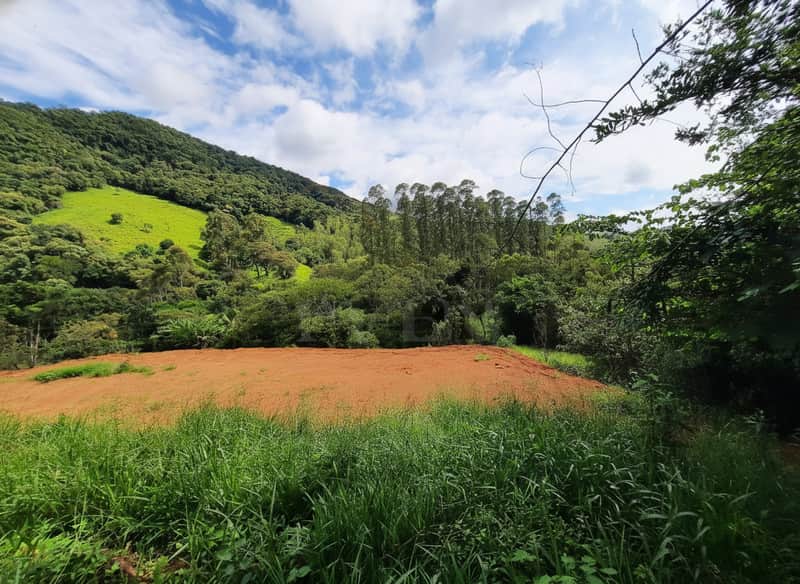 Área externa com terraplanagem e vegetação. Montanha verde ao fundo sob céu azul com nuvens.