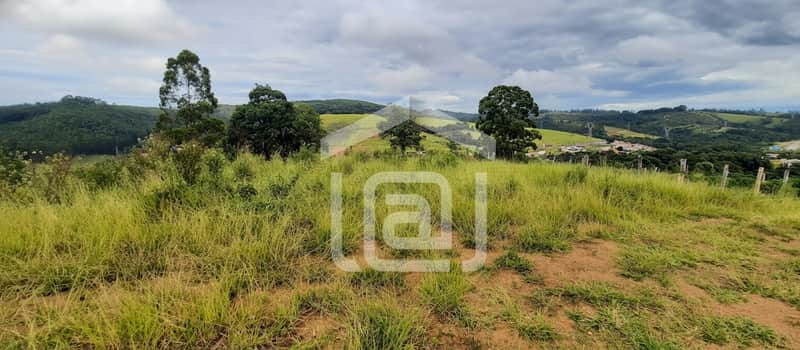 Terreno gramado com árvores e vista panorâmica de morros e céu nublado. Área externa ampla e natural.