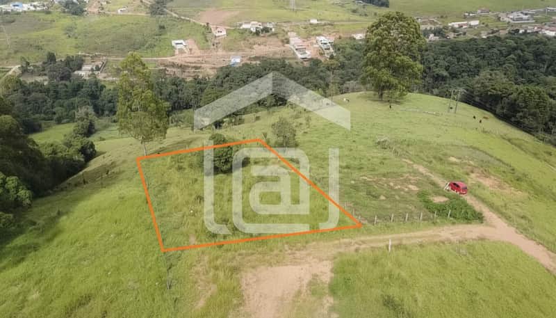 Terreno gramado com cerca e vegetação. Vista panorâmica de morros e área urbana ao fundo. Ideal para construção.