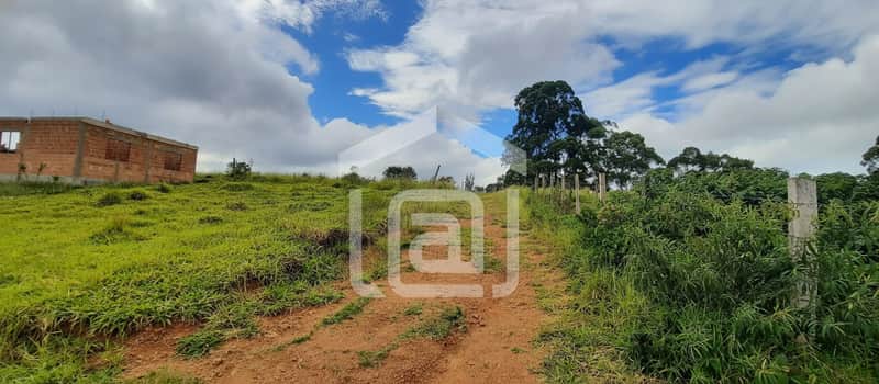 Terreno gramado com construção inacabada ao fundo e árvores. Céu azul com nuvens.