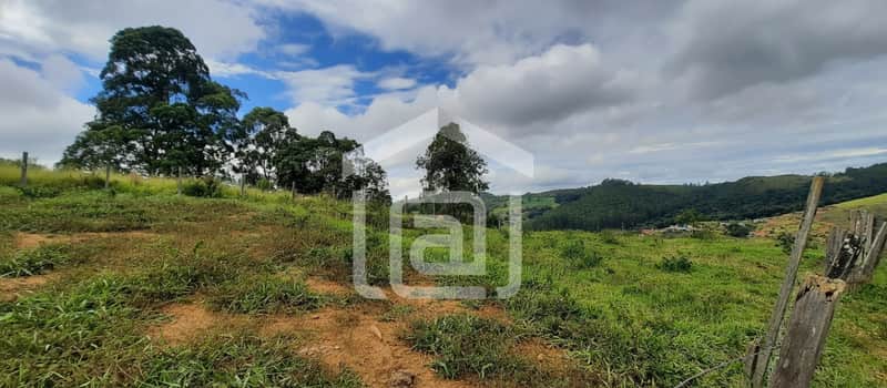 Terreno gramado com árvores e cerca de madeira. Vista para montanhas e céu nublado.