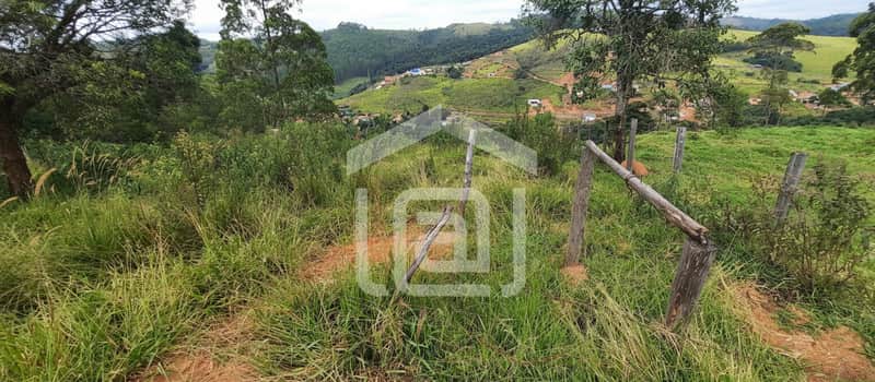 Terreno rural com cerca de madeira, vegetação abundante e vista para montanhas.