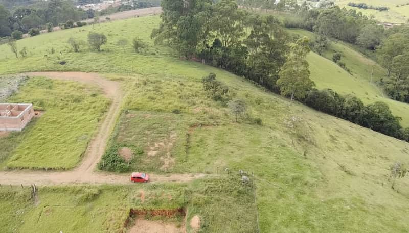 Terreno verde com casa em construção e carro vermelho. Vista panorâmica rural.