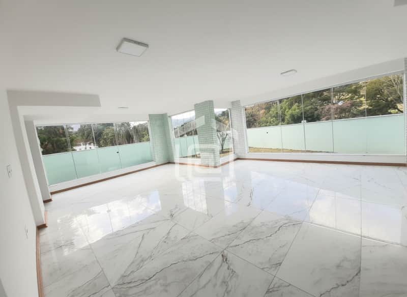 Sala ampla com piso de mármore, paredes brancas e janelas grandes com vista para área verde.