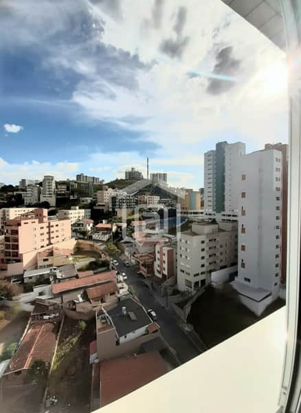 Vista da janela de apartamento. Prédios, casas e céu azul com nuvens em dia ensolarado.