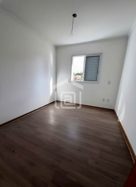 Quarto vazio com piso amadeirado e janela com persiana. Paredes brancas e ponto de luz no teto.