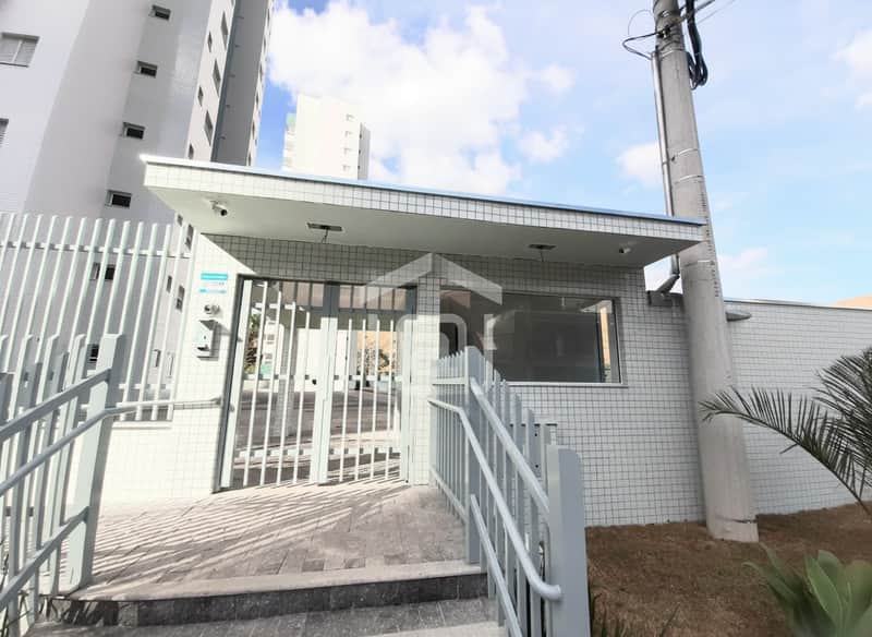 Fachada de prédio com portaria gradeada e guarita revestida em azulejos claros. Acesso com rampa e corrimão.