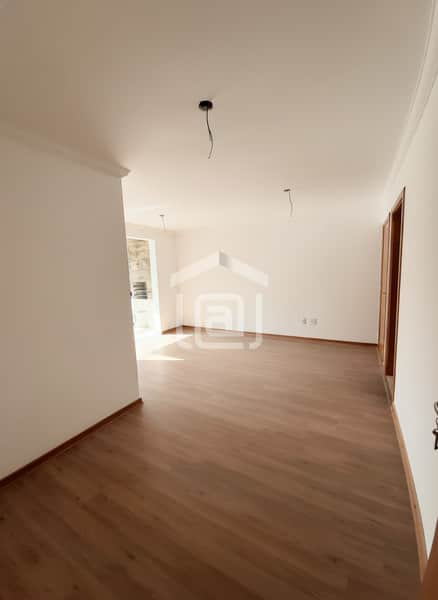 Sala ampla e clara com piso amadeirado. Paredes brancas e fiação aparente no teto. Ambiente arejado.
