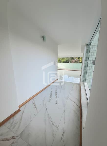 Corredor claro com piso de mármore, parede branca e janela envidraçada. Ambiente iluminado e moderno.