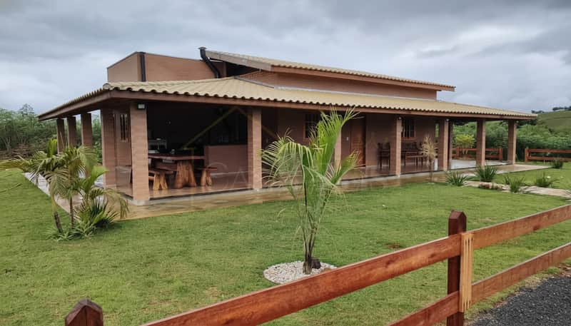 Casa térrea com varanda, jardim gramado e cerca de madeira. Arquitetura rústica, ambiente campestre.