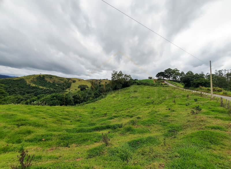 Paisagem rural com colinas verdejantes sob céu nublado. Estrada sinuosa ao lado. Natureza exuberante.