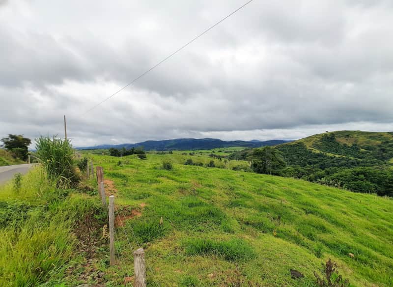 Paisagem rural com colinas verdes, cerca de madeira e céu nublado. Natureza exuberante e tranquila.